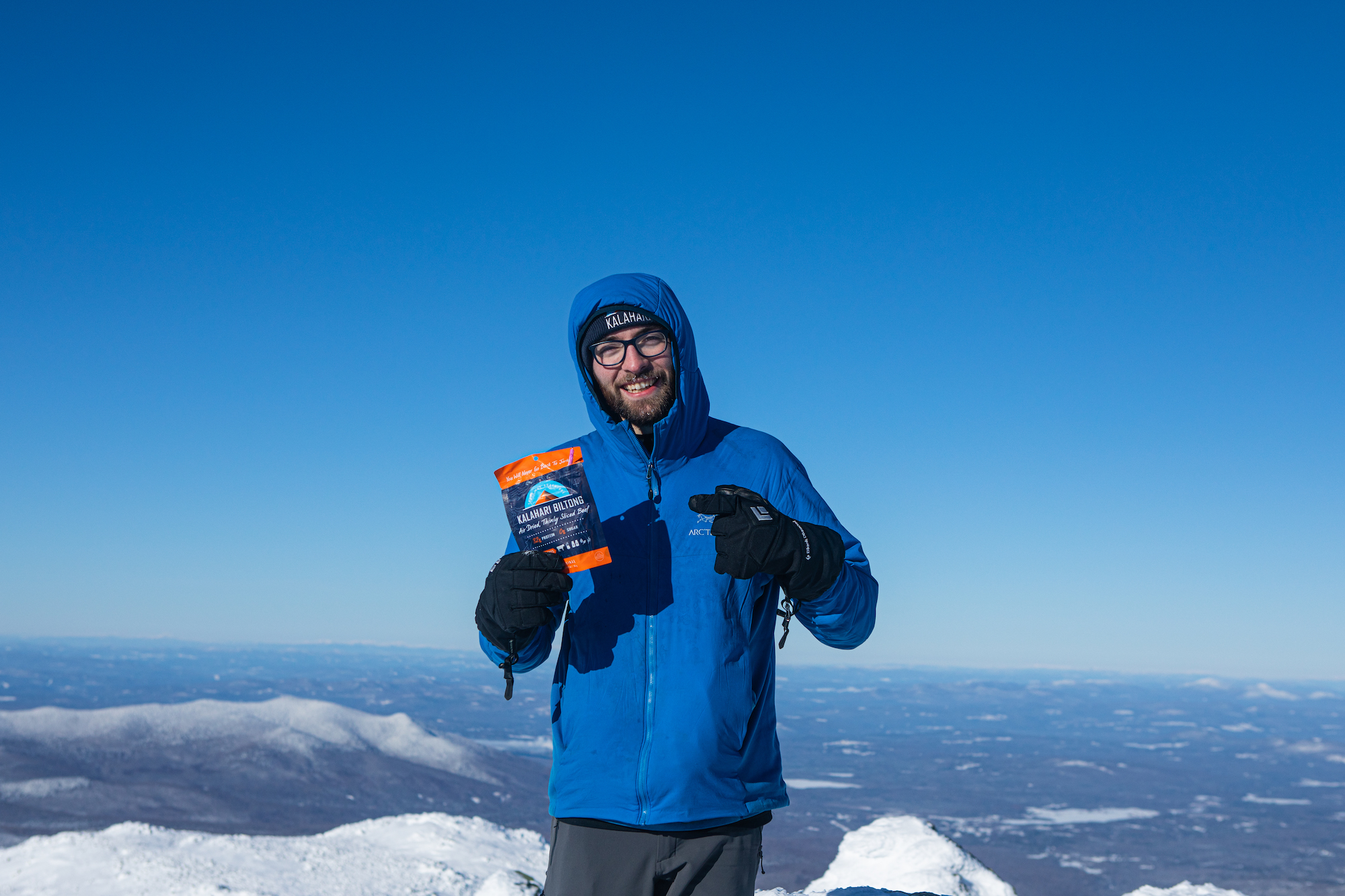 man with blue jacket stands on mountain top with bag of Kalahari in hand