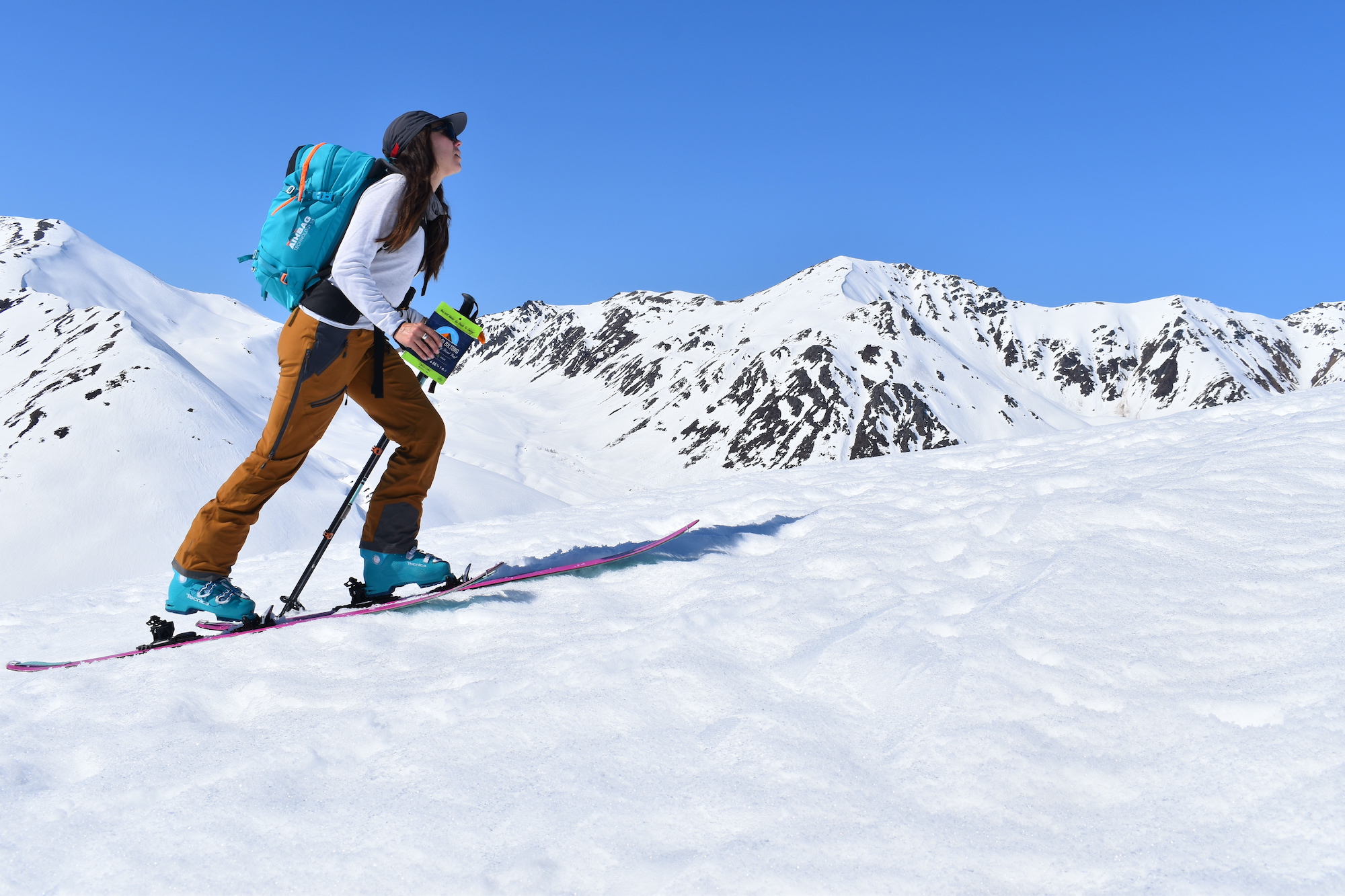 woman traverses mountain on skis with backpack holding a bag of biltong