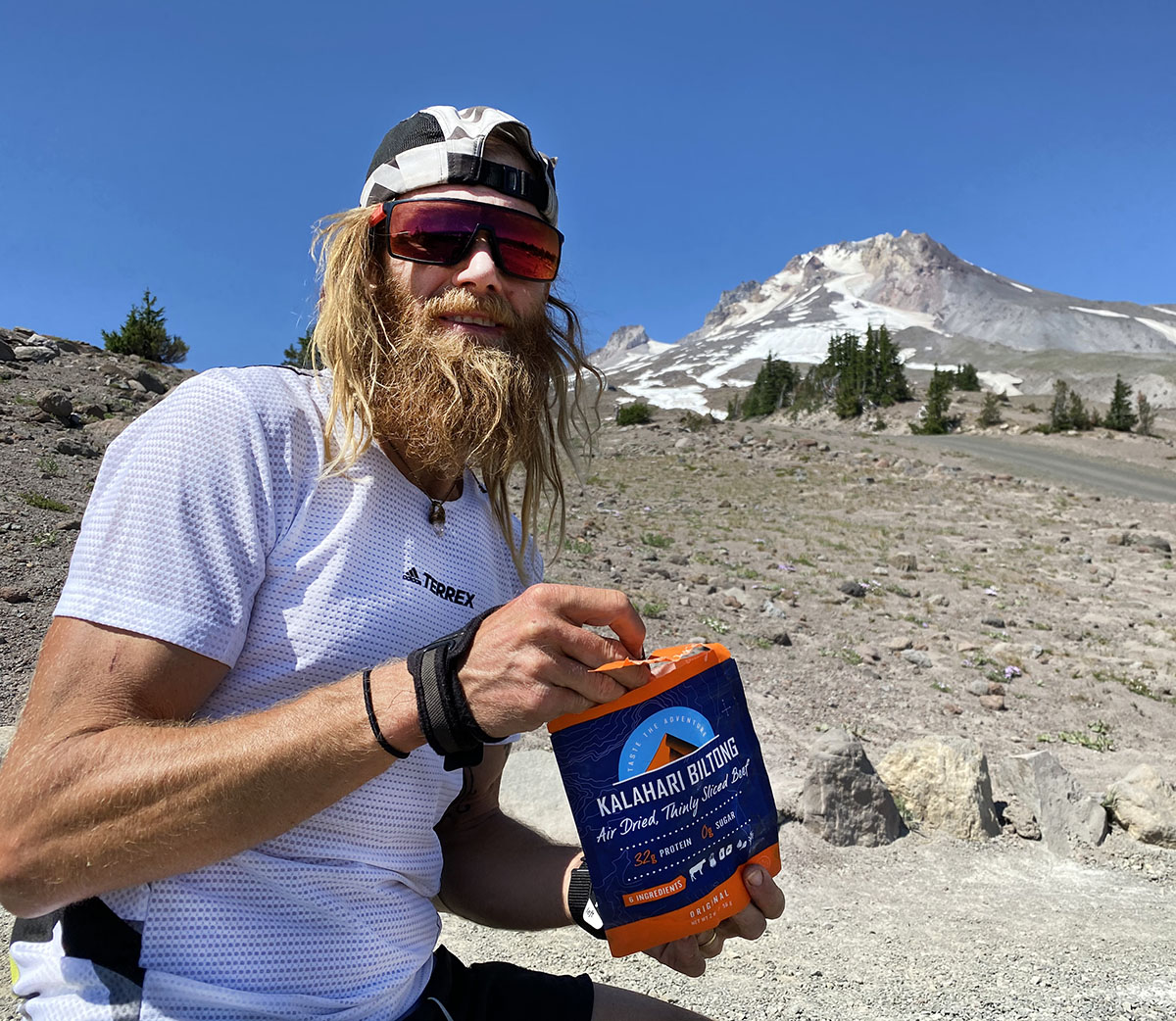 Timothy Olson eating original biltong with snow topped mountain in the background