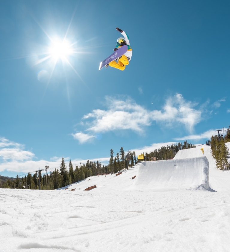 Summer Fenton grabbing her snowboard mid air in front of a large jump