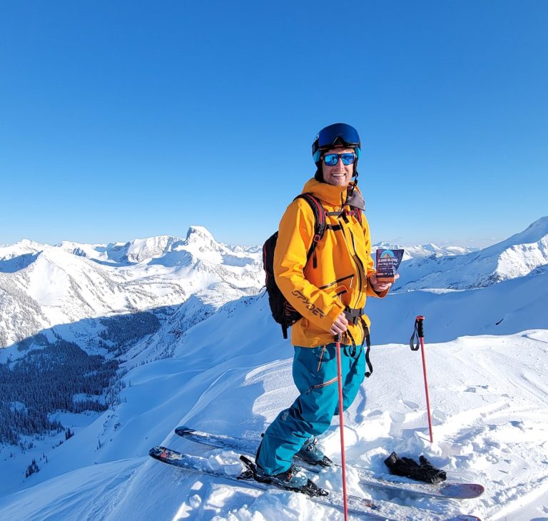 Man on downhill skis standing on top of a mountain holding Kalahari biltong