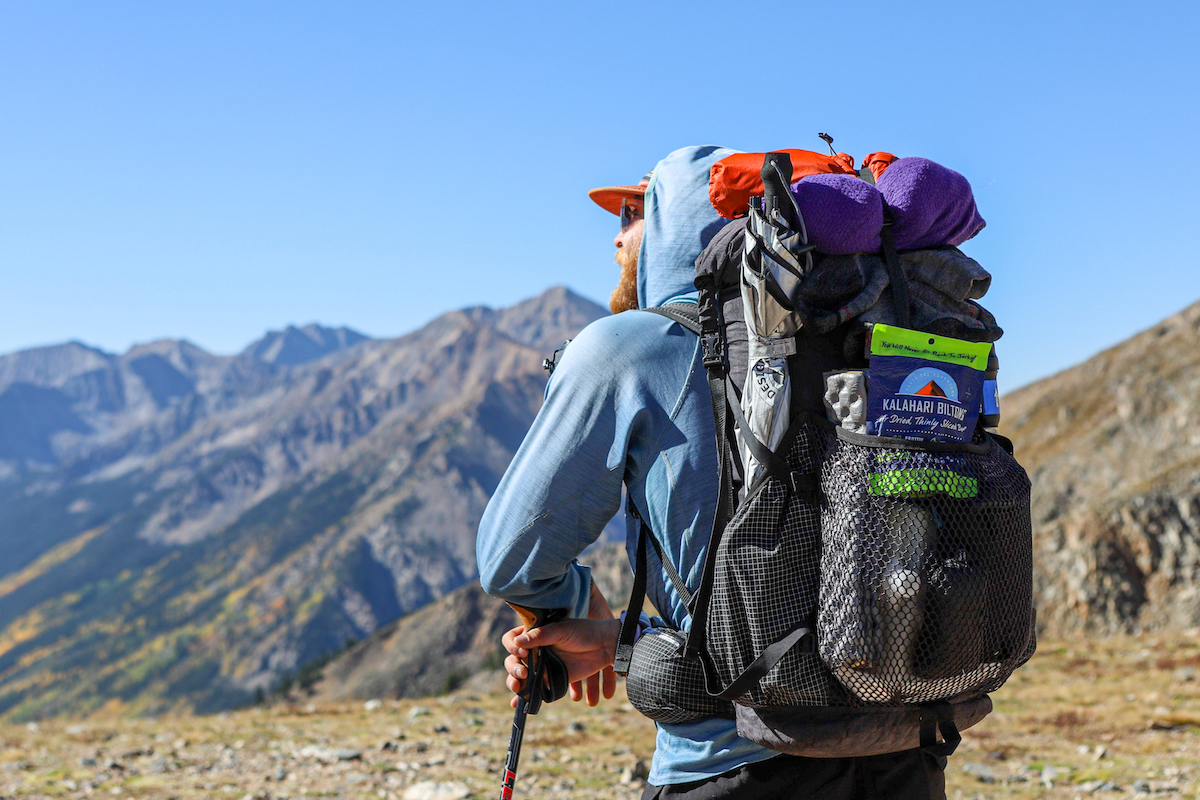 Man faces mountains with large backpack, Lime Chili Biltong is visible in the outer pocket